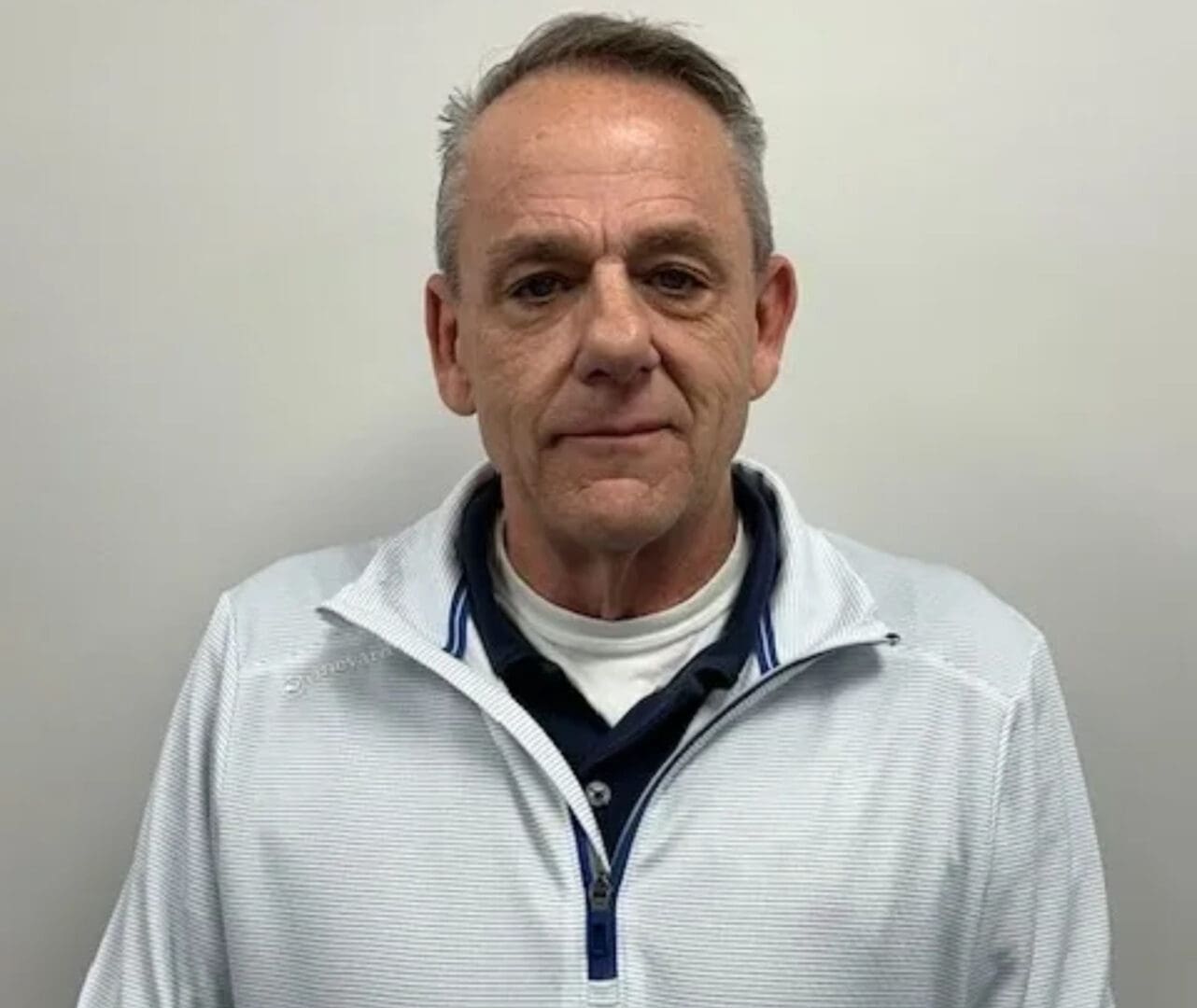 A man in white shirt and blue jacket standing next to wall.